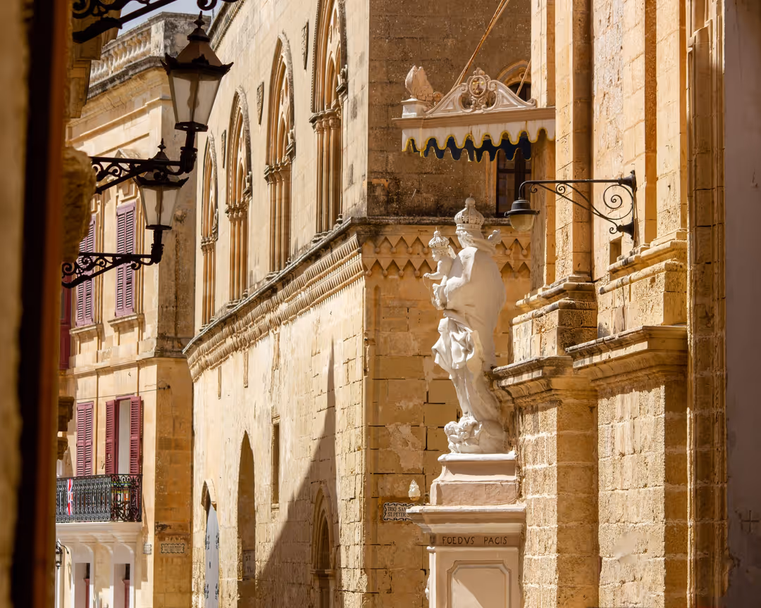A golden limestone street in Mdina with lanterns and a statue